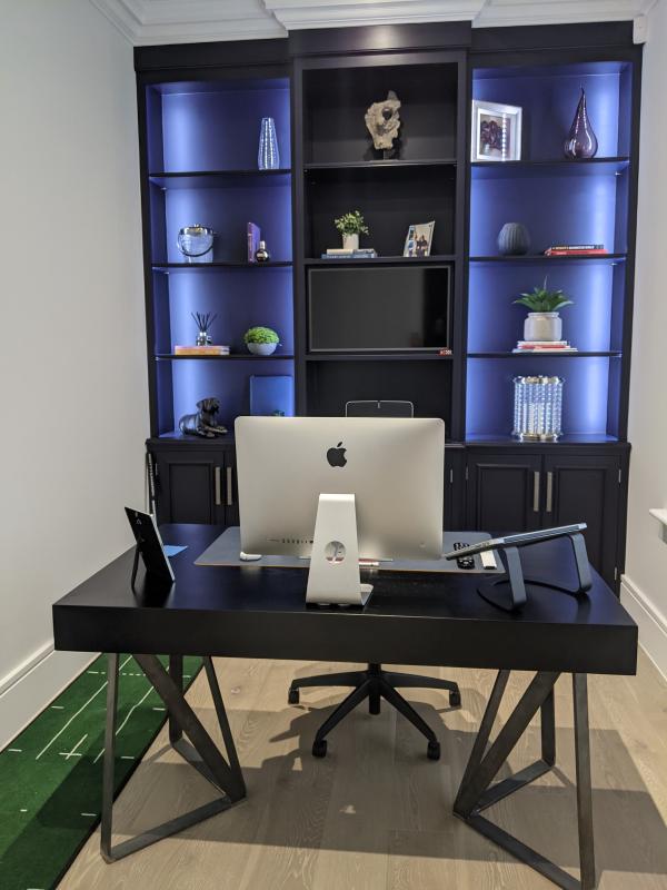 a mans study area or home office with led lit bookcase and Apple Mac computer on desk